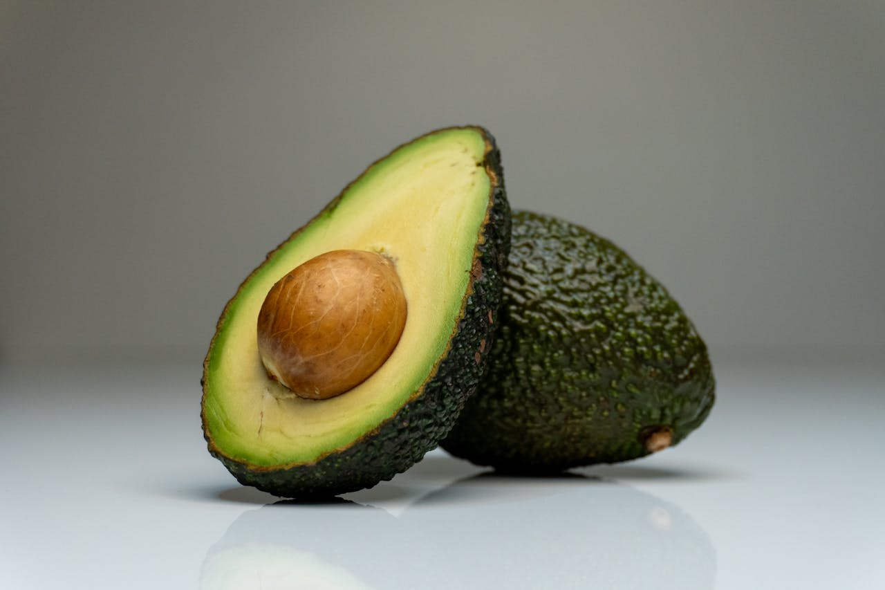 Close-up of a halved avocado with seed, showcasing vibrant colors on a reflective white background.