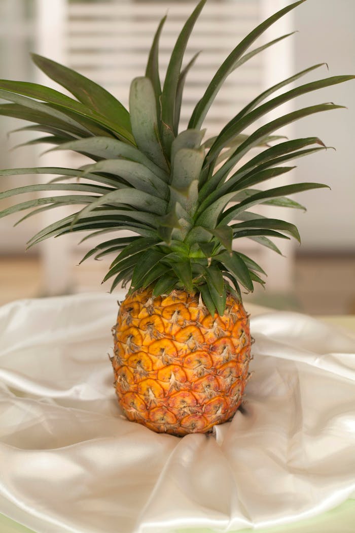 A vibrant pineapple displayed on a soft white satin, showcasing its beautiful texture and color.