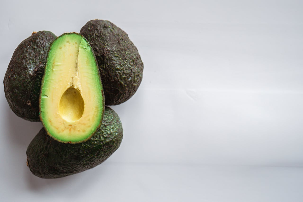 Top view of heap of fresh avocados with rough dry skin and colorful tender pulp on white background